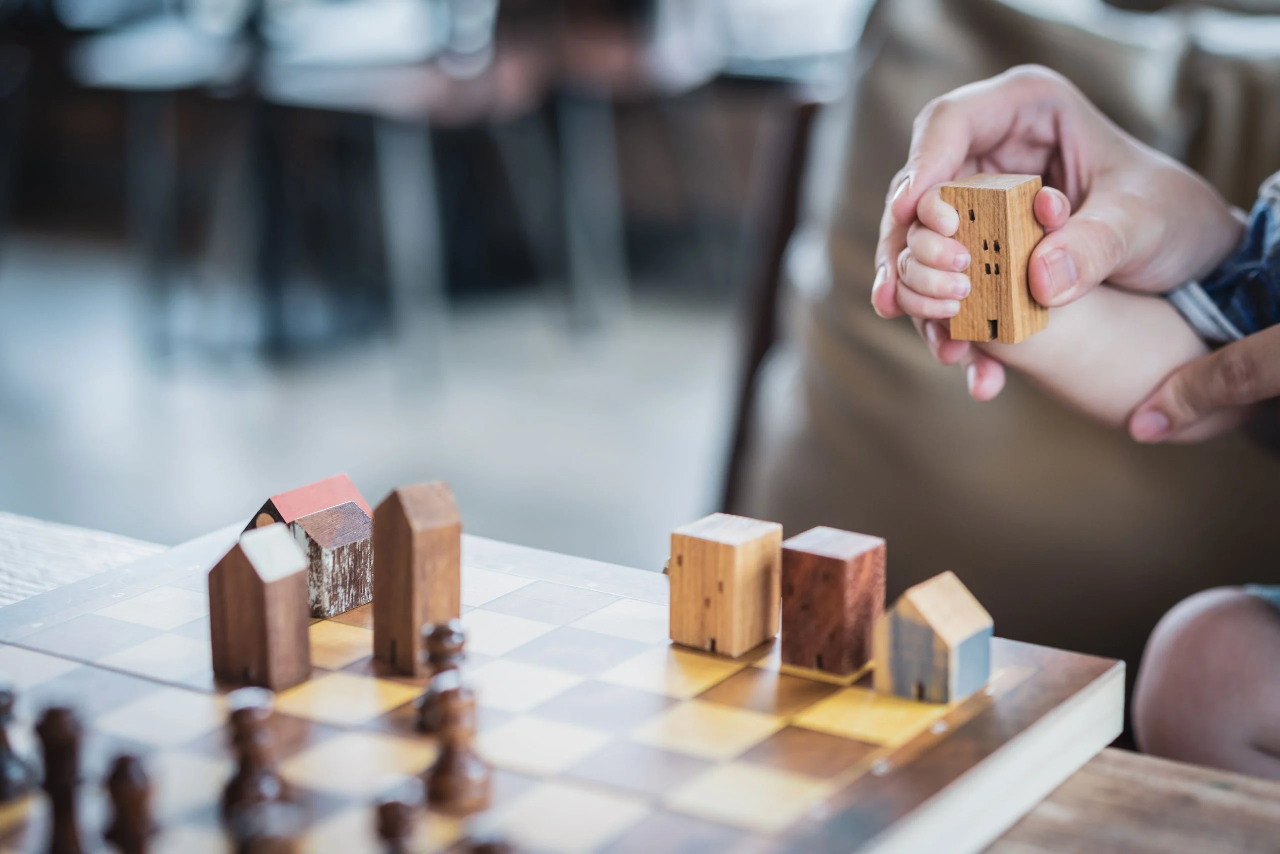 Wooden model houses on a board, with an adult's hand guiding a child's